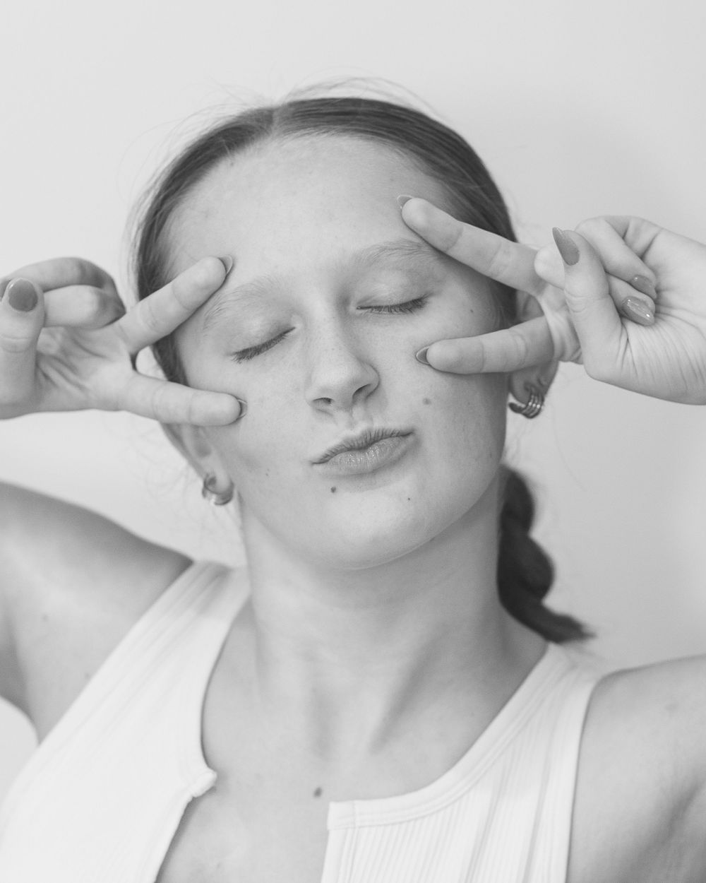 Black and white portrait showing person making peace signs near eyes with relaxed expression at home studio