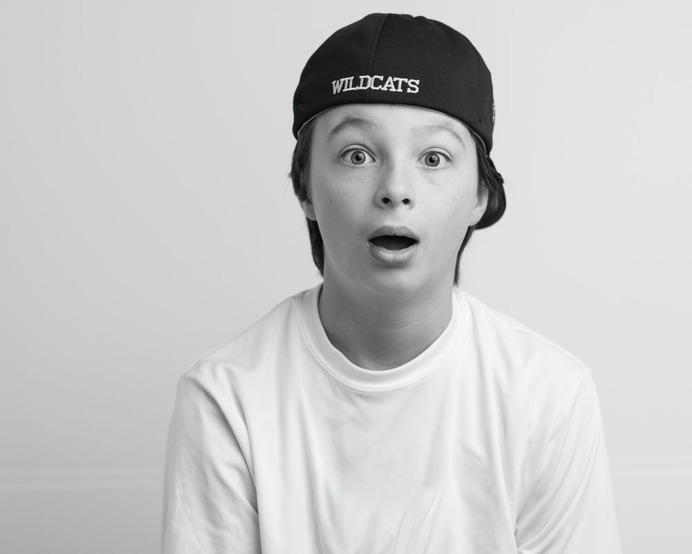 Black and white studio portrait showing excited expression while wearing Wildcats cap and white t-shirt at home studio