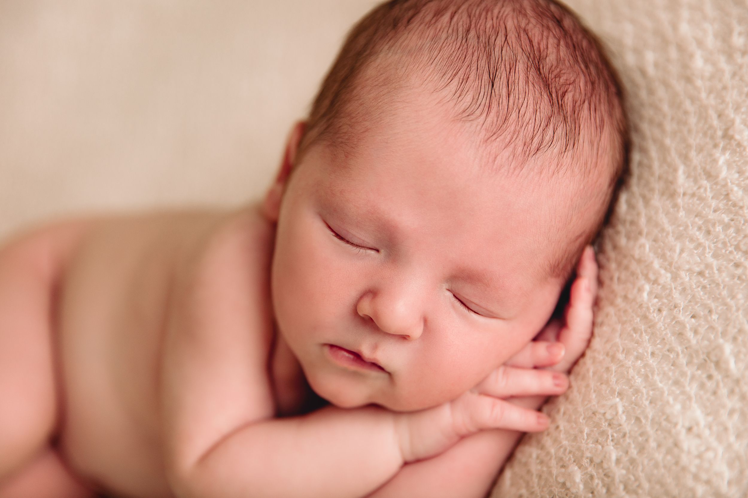 close up newborn boy sleeping hands resting under cheek