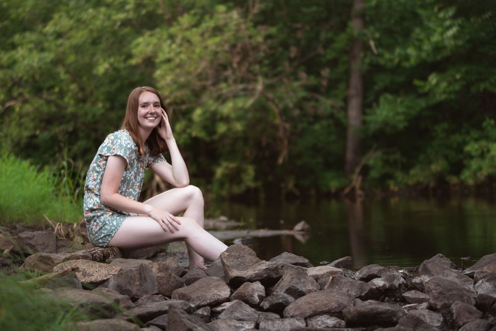 Girl with red hair sitting on rocks of a creek