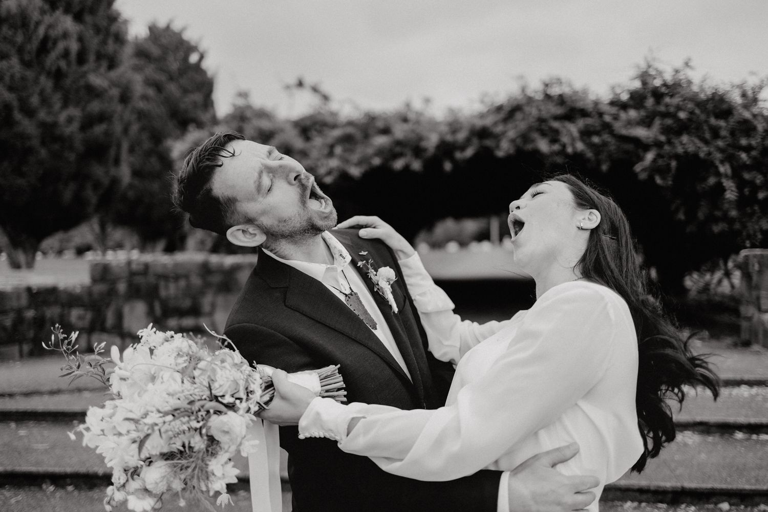 A black and white photo captures a joyful laughing moment at a wedding.