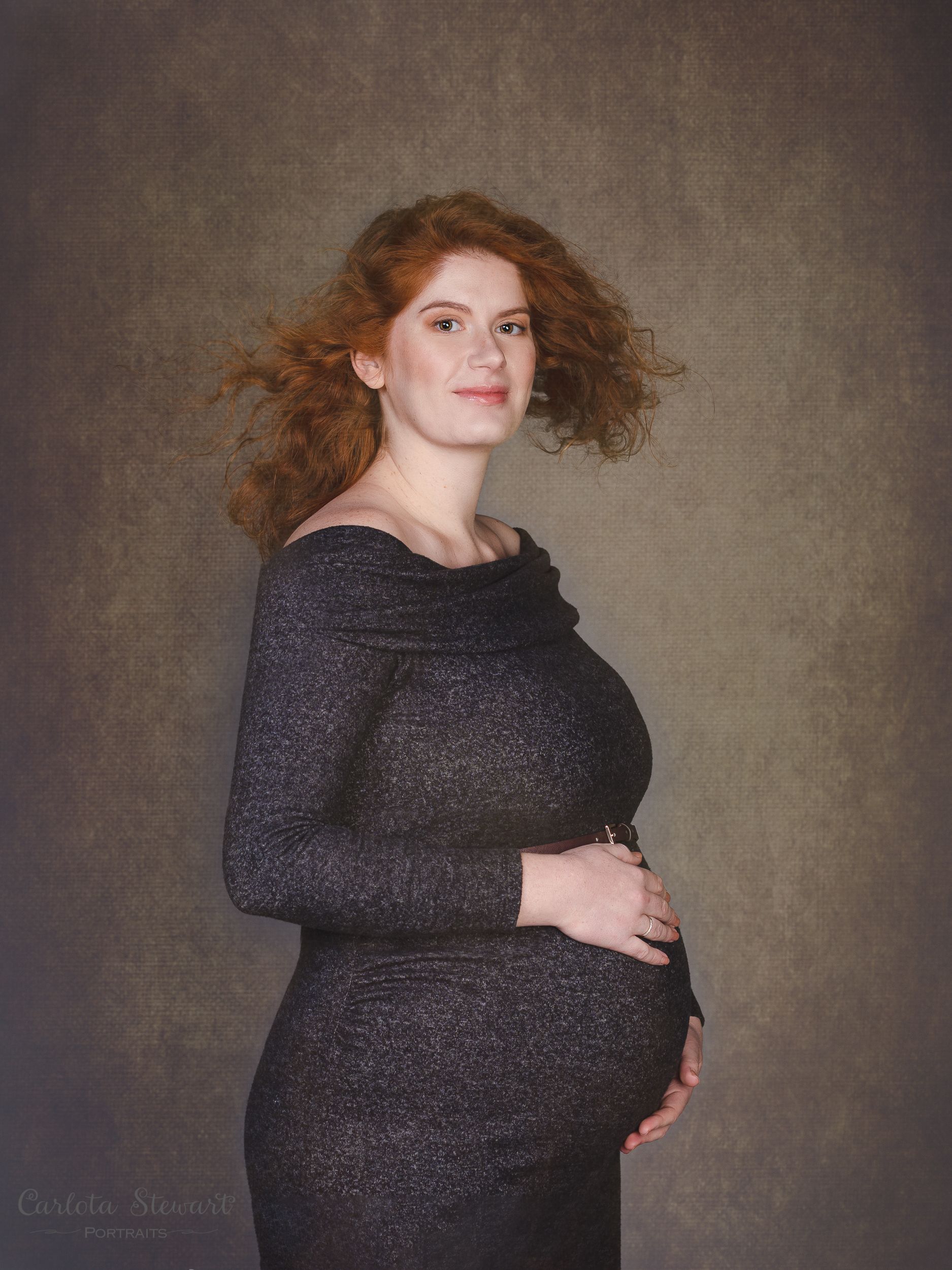 Photo of expectant mother wearing a grey dress looking at the camera.