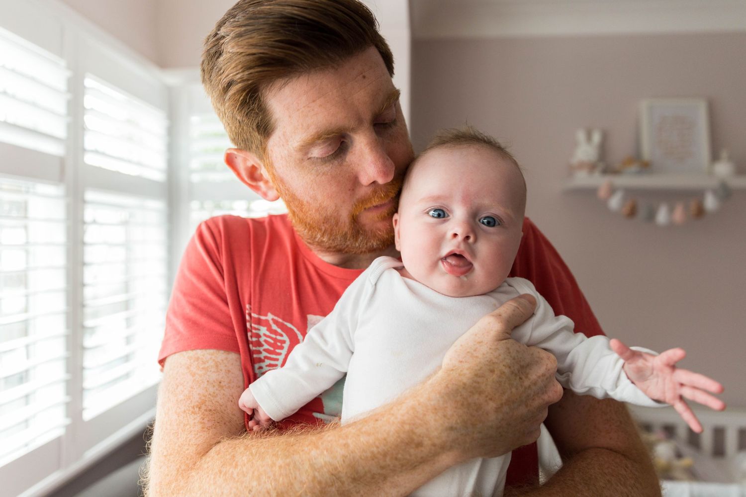 dad in red t-shirt holding baby girl against his chest