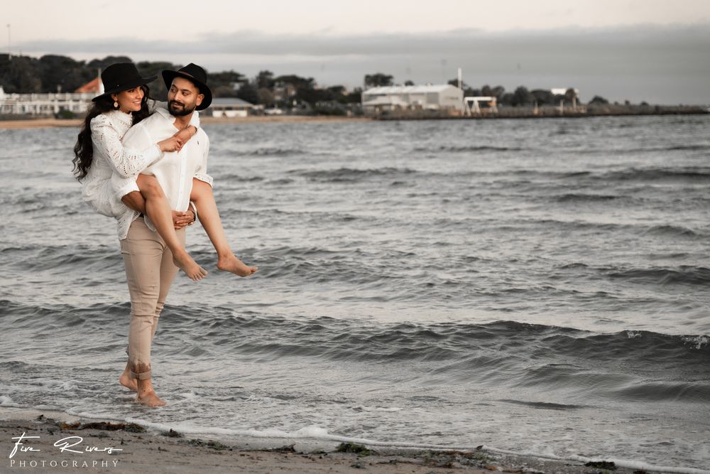 Couple in coordinated white outfits enjoying playful moment at water's edge during sunset.
