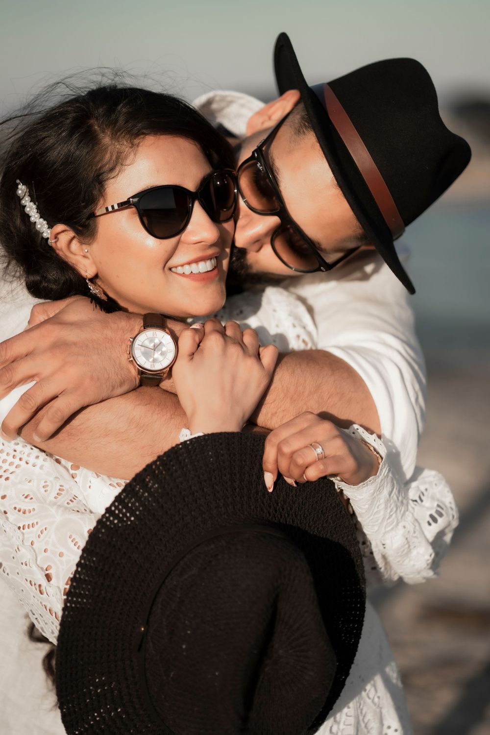 Intimate beach portrait of couple with hats and sunglasses sharing tender moment.