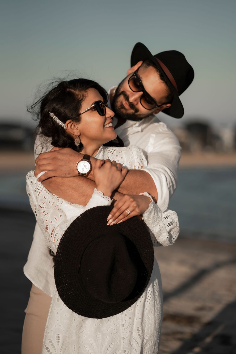 Candid beach portrait of laughing couple in white outfits and fashionable accessories.