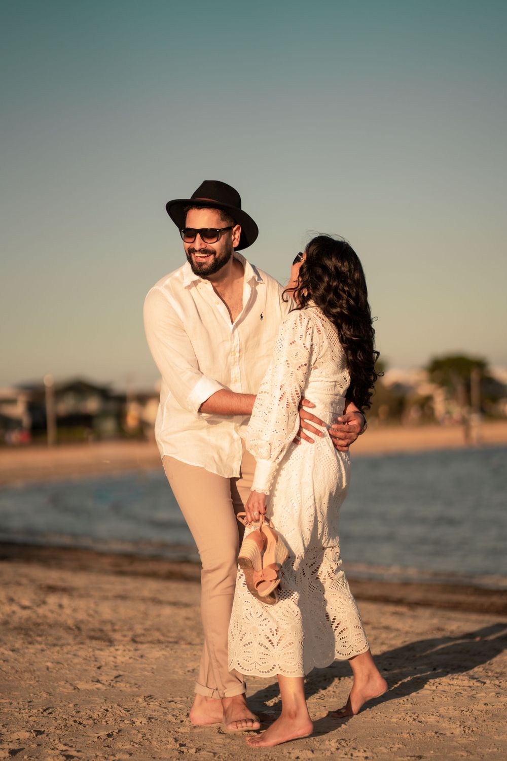 Stylish couple in matching light-colored outfits sharing intimate moment on beach at golden hour.