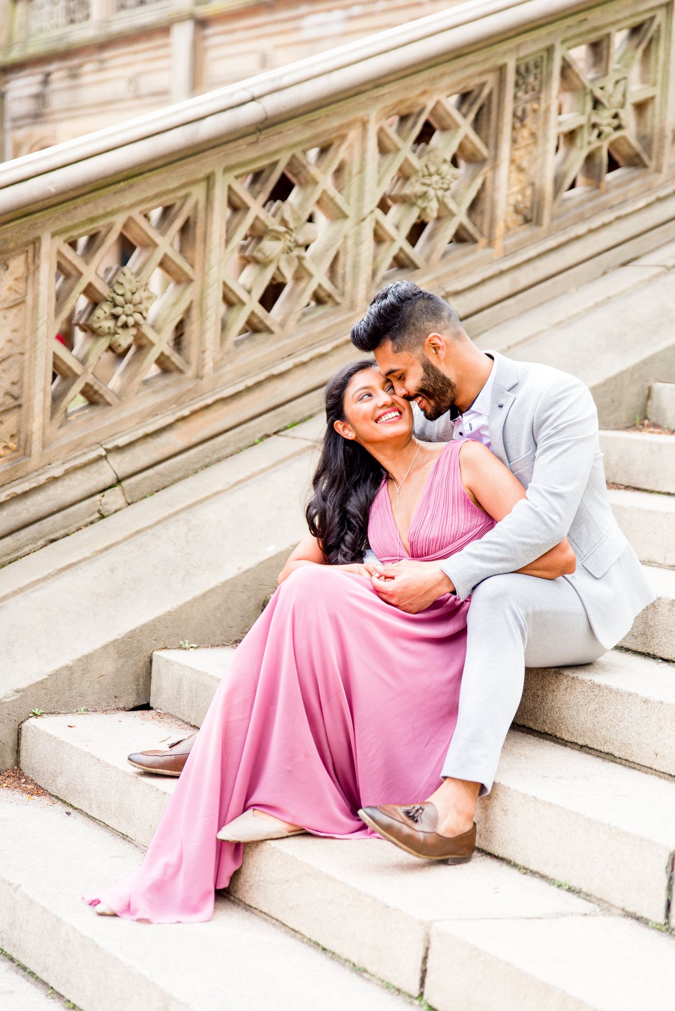 woman in pink dress and man in grey suit sitting on Bethesda Terrace steps and laughing with each other at Central Park