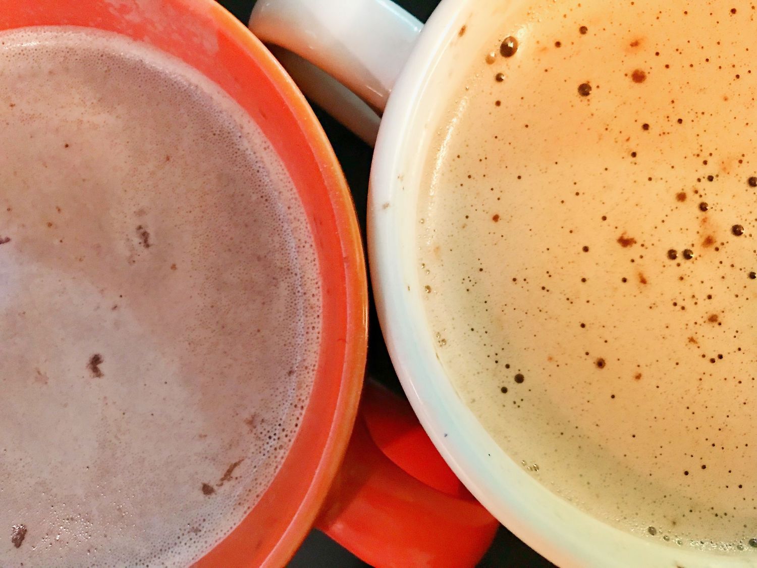 Two cups of frothy hot chocolate shown from above, one light and one dark colored.