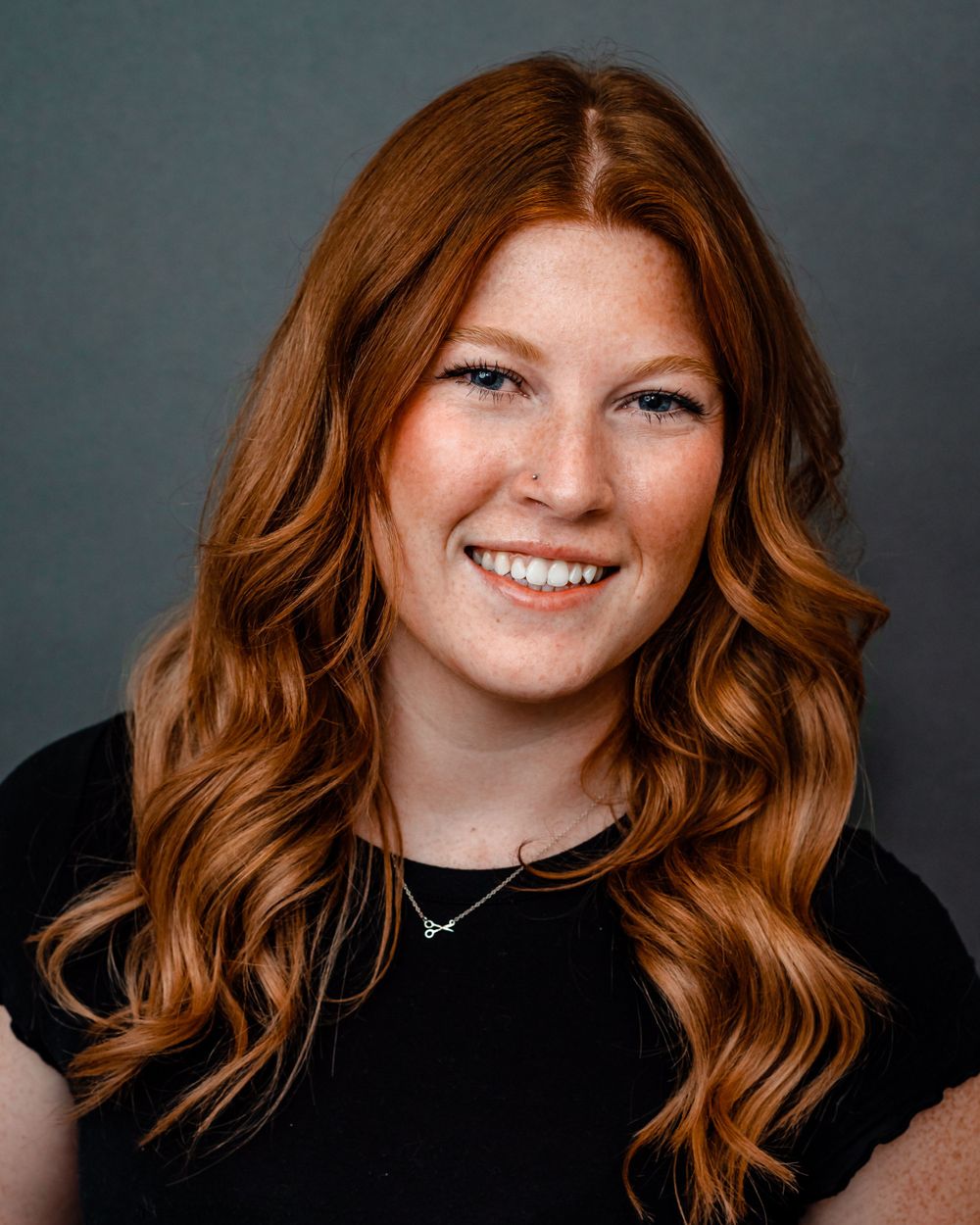 Professional headshot of a woman with flowing red hair wearing black against a gray background.