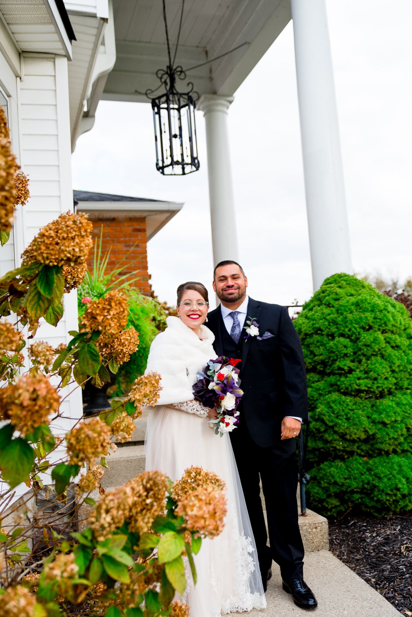 bride and groom hugging and smiling outside white house and brown hydrangea bush in Ohio