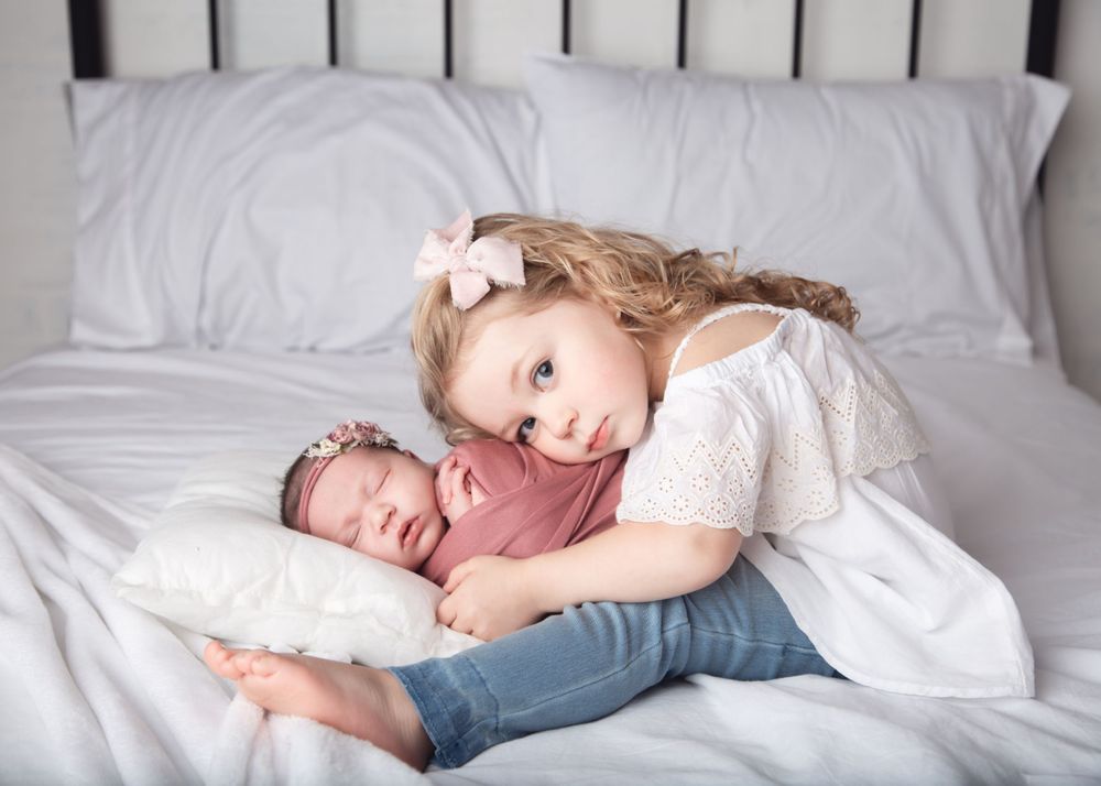 Newborn baby with sister laying on bed - Newborn photographer in Penticton