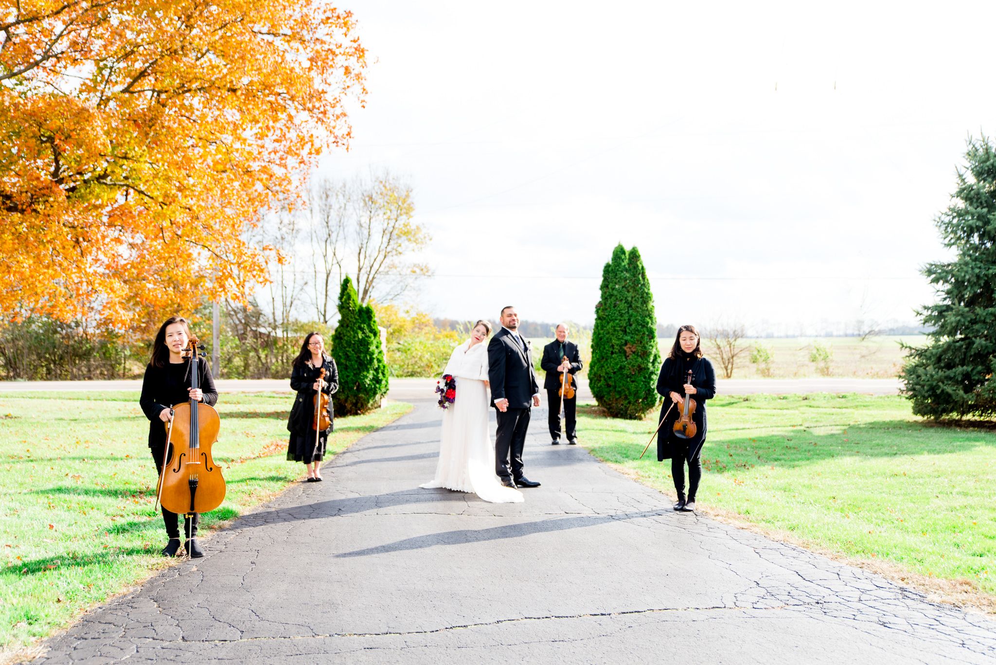 bride and groom standing back to back with string quartet staggered on either side in front of orange tree