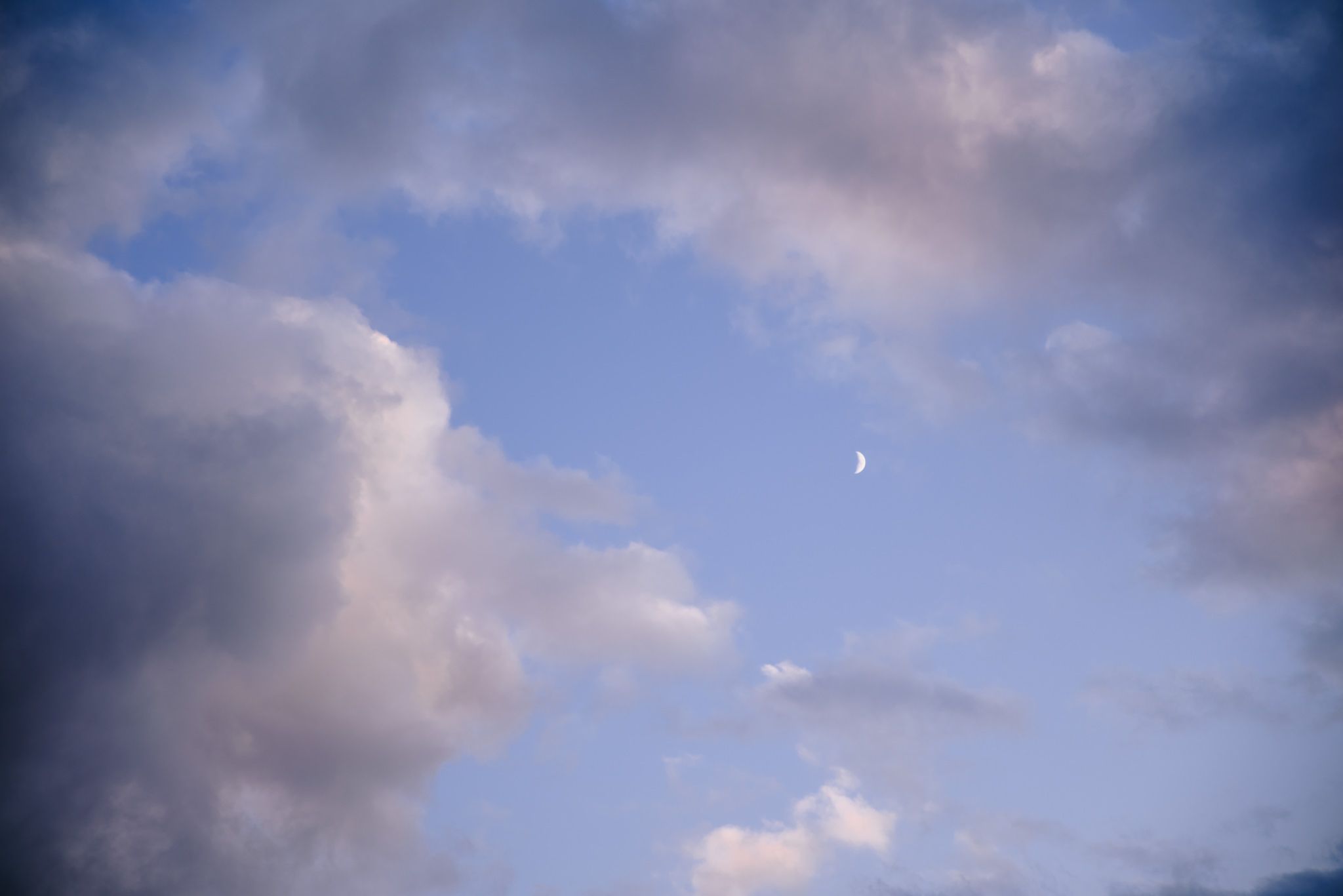 sliver of moon showing through clouds in a light blue sky at an outdoor cold barn wedding in November in Ohio