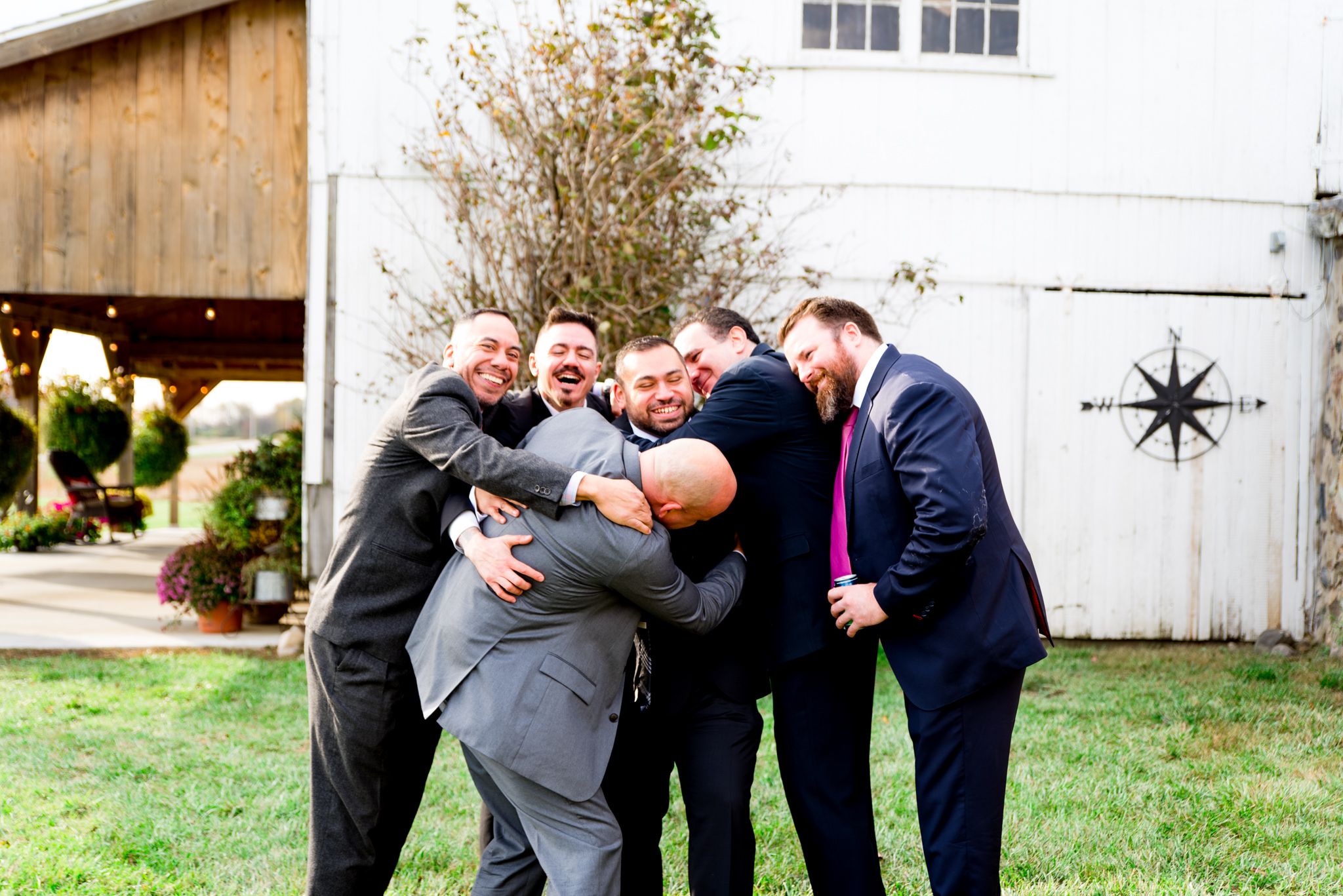 group of 6 men hugging at the groom's outdoor fall wedding in Chicago in front of white barn