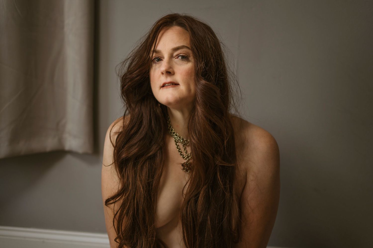 A woman with her dark brown hair hanging down to cover her breasts wearing a chainmail necklace