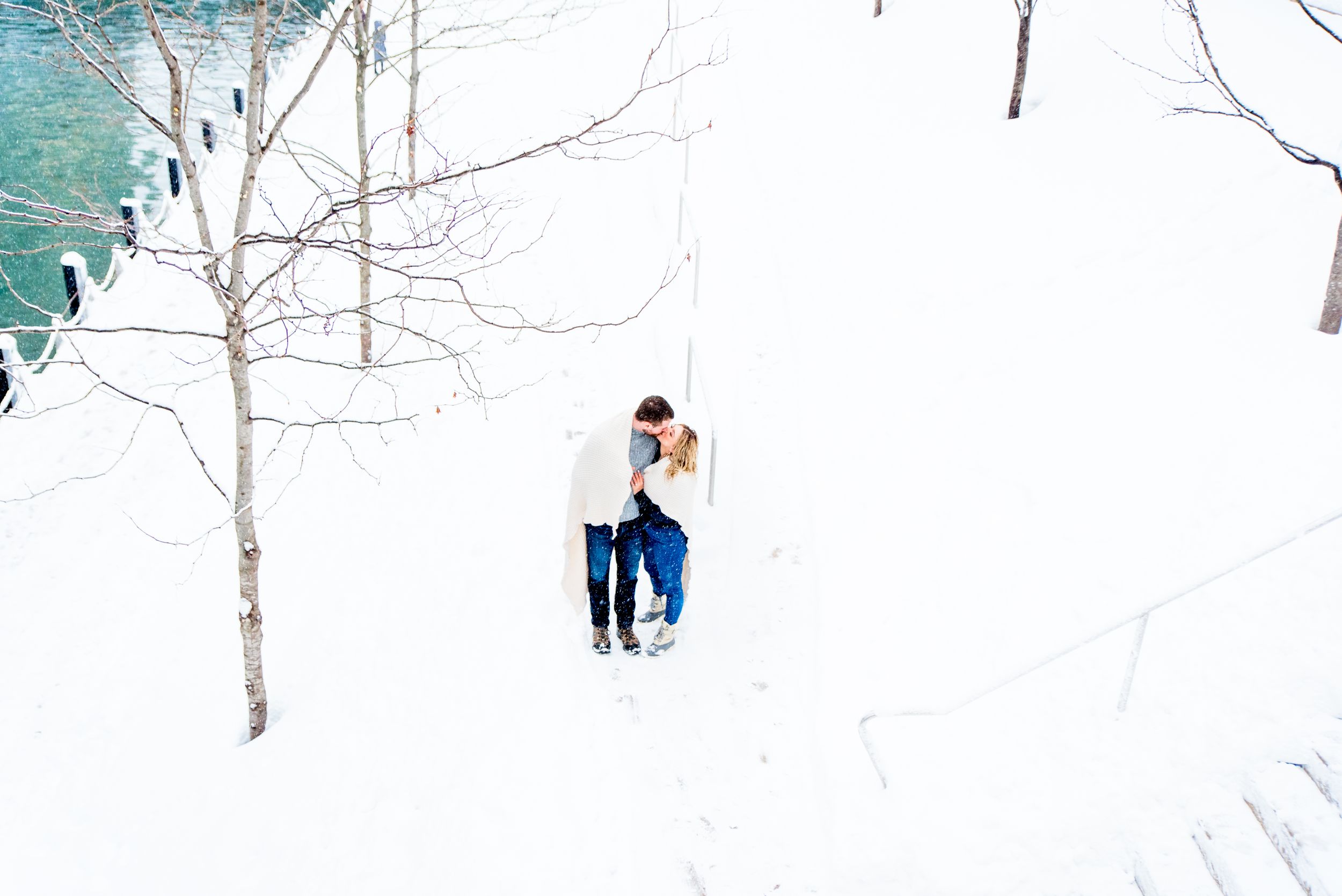 young engaged couple wrapped in blanket on the stairs at Chicago Riverwalk for snowy engagement pictures in Chicago