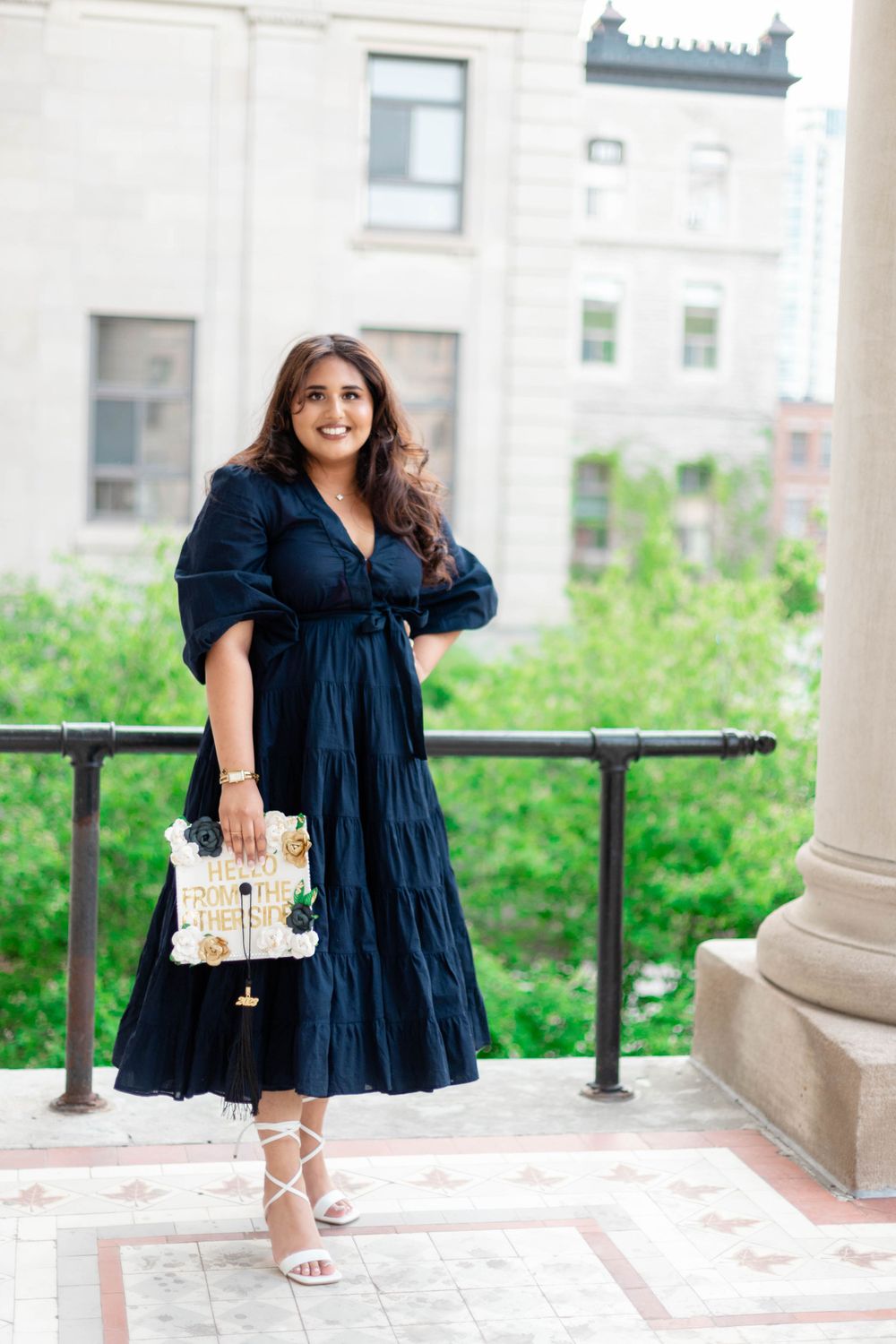 Stylish woman in navy tiered maxi dress poses outdoors against architectural backdrop with small handbag.