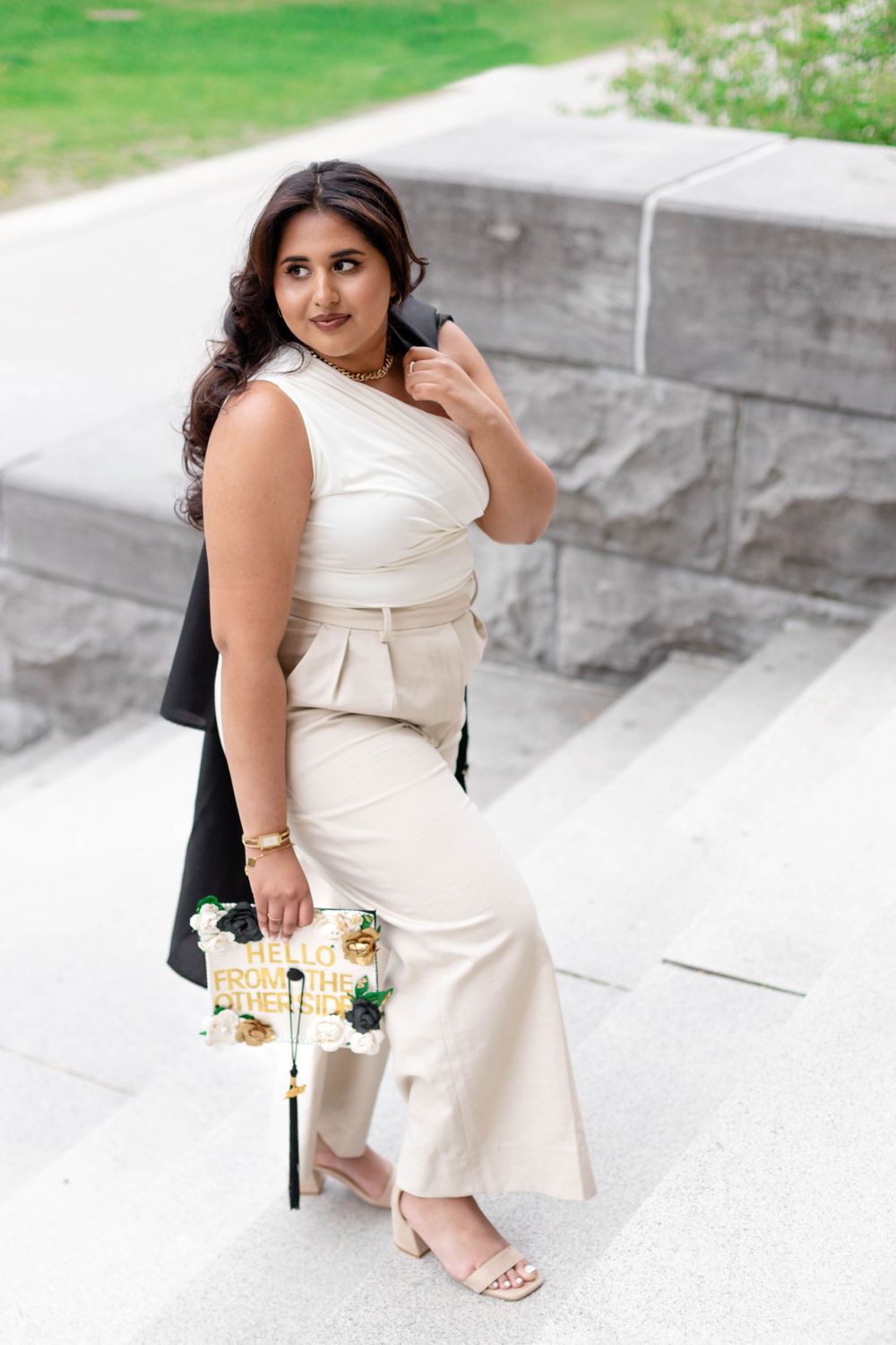 Woman in elegant cream outfit with coordinated purse poses on stone steps outdoors.