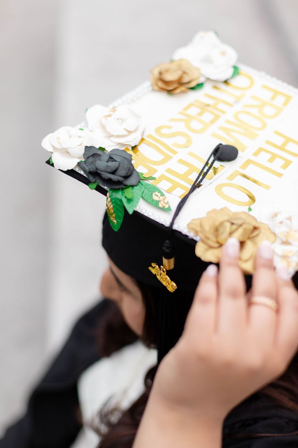 Decorated graduation cap with white and gold flowers and text details shown in close-up.