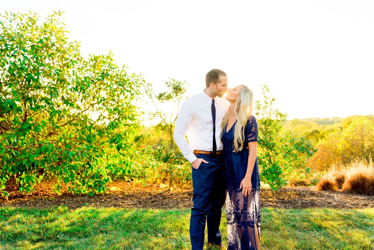 husband and wife in white and navy clothes kissing at sunset