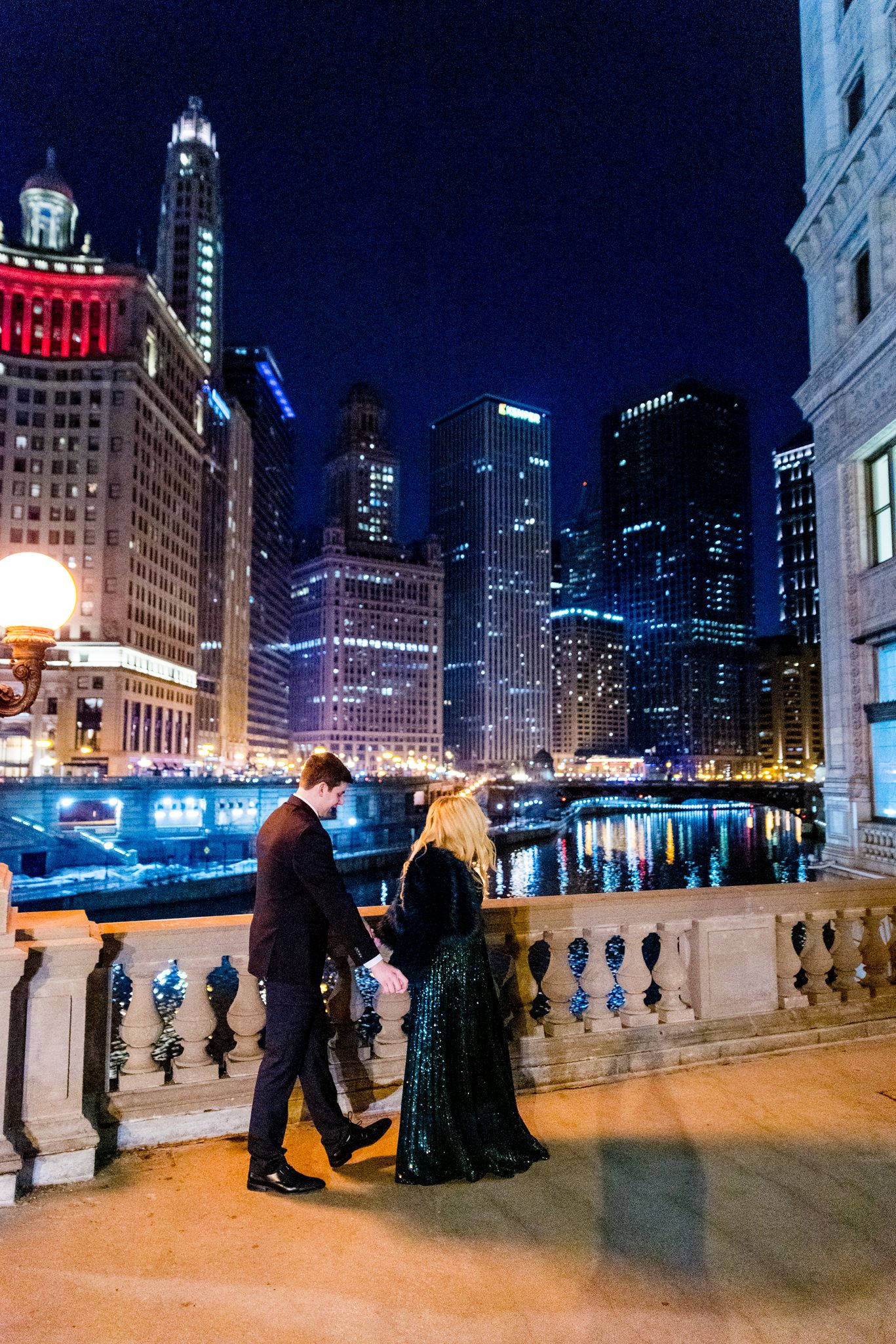 woman in sparkly green dress walking with man near the Wrigley Building for Chicago engagement pictures at night