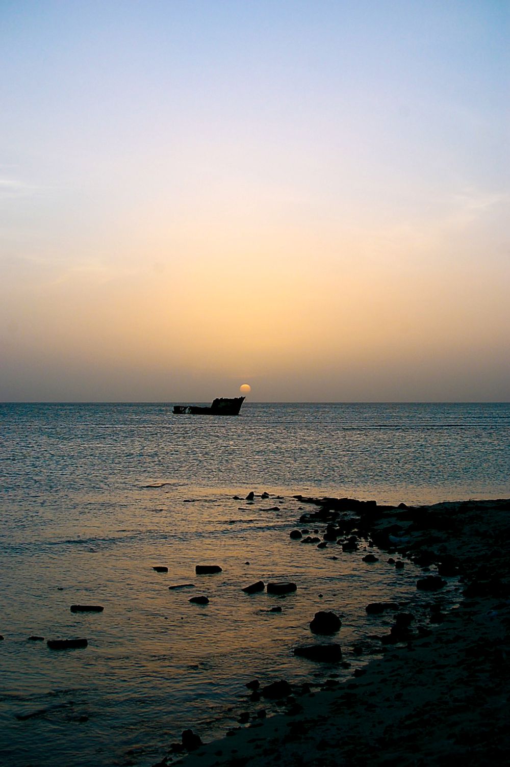 Silhouette of a shipwreck on the horizon during sunset over calm waters.