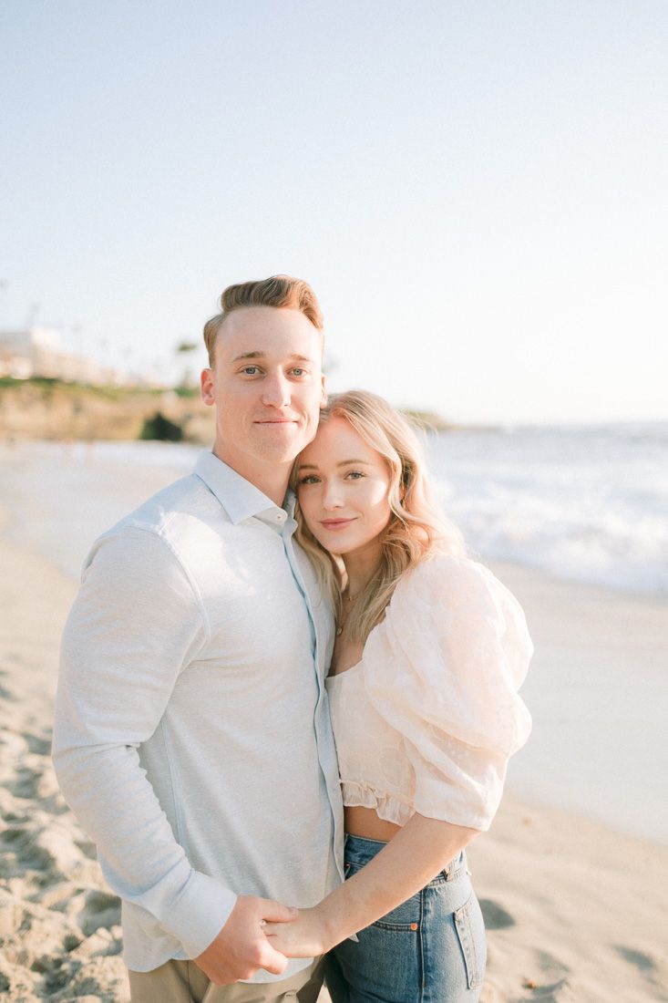 A romantic couple embracing on a sandy beach with coastal cliffs in the background.