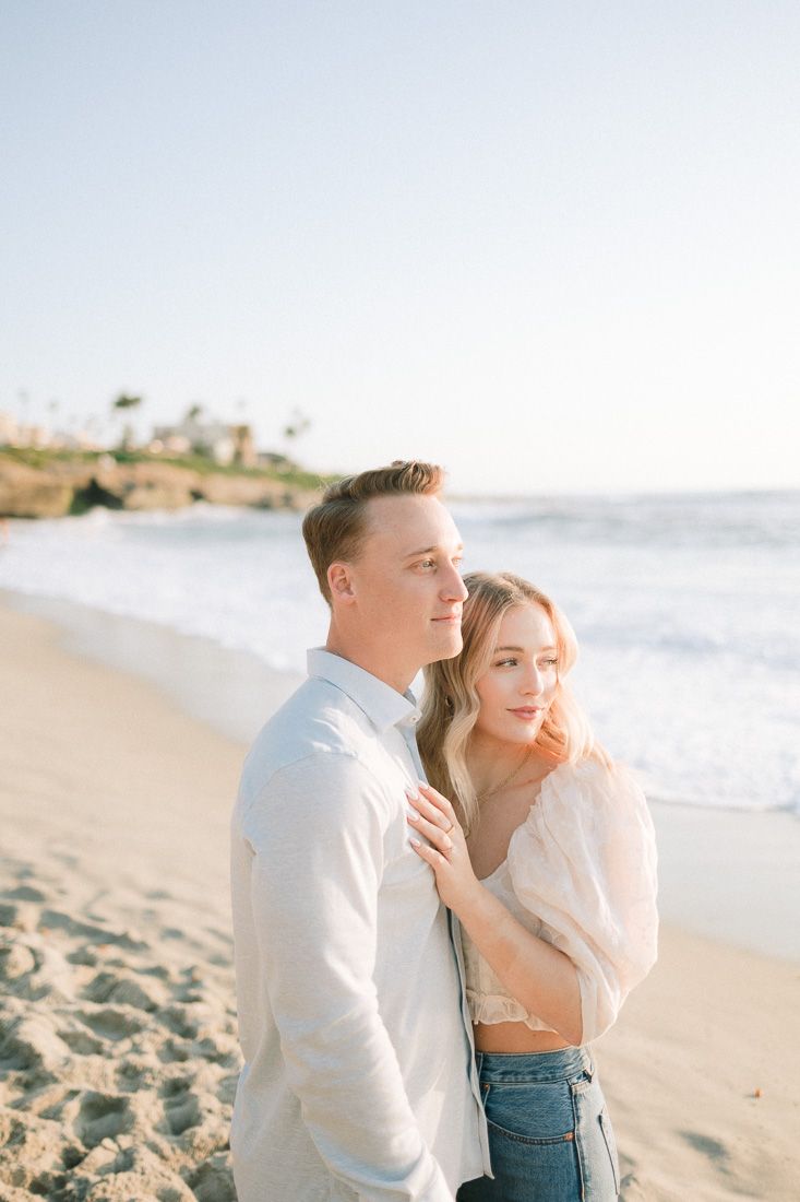 A couple in casual attire posing together on a beach during golden hour.