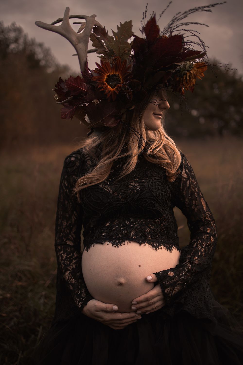 Ethereal maternity photo featuring black lace dress and dramatic floral crown with sunflowers against moody autumn backdrop.