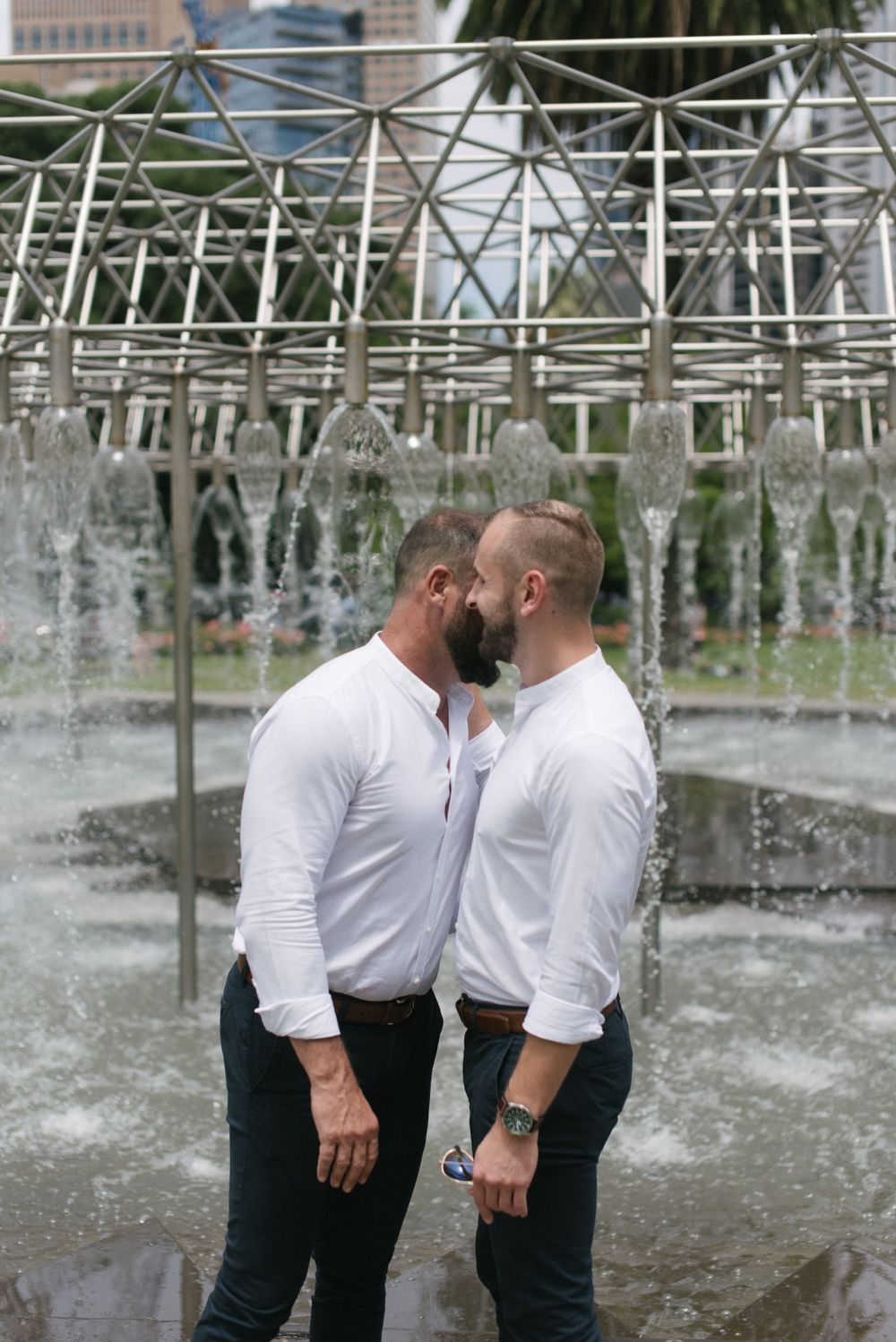 Two people share an intimate moment by a modern water feature.