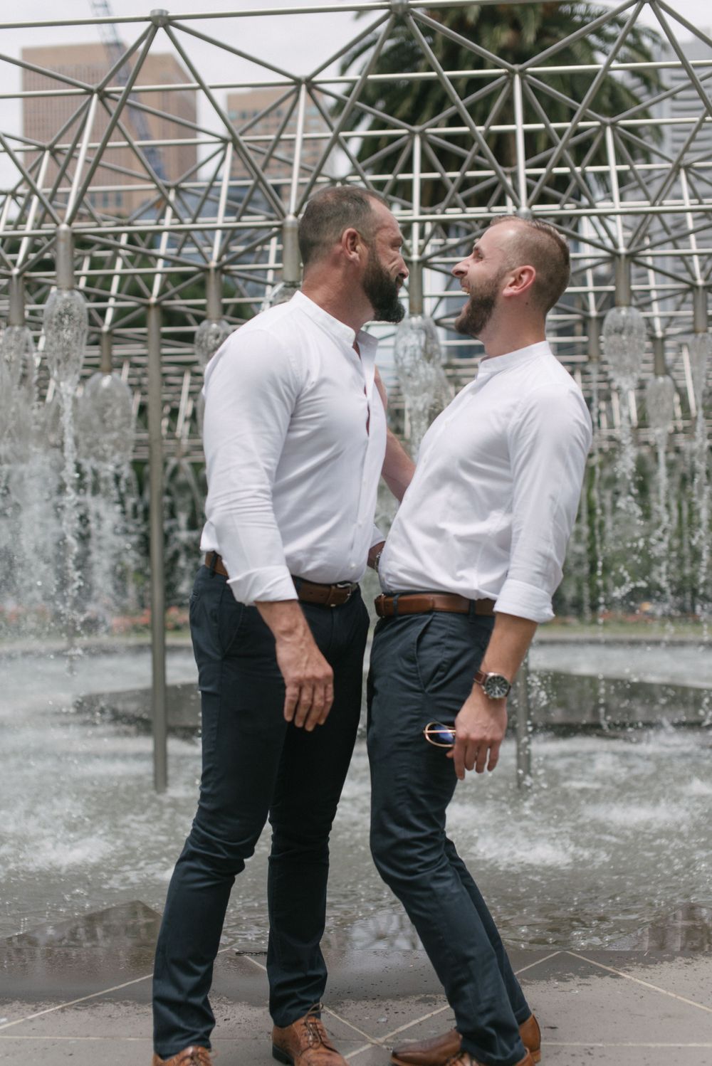 Couple in matching white shirts pose intimately by geometric fountain structure.
