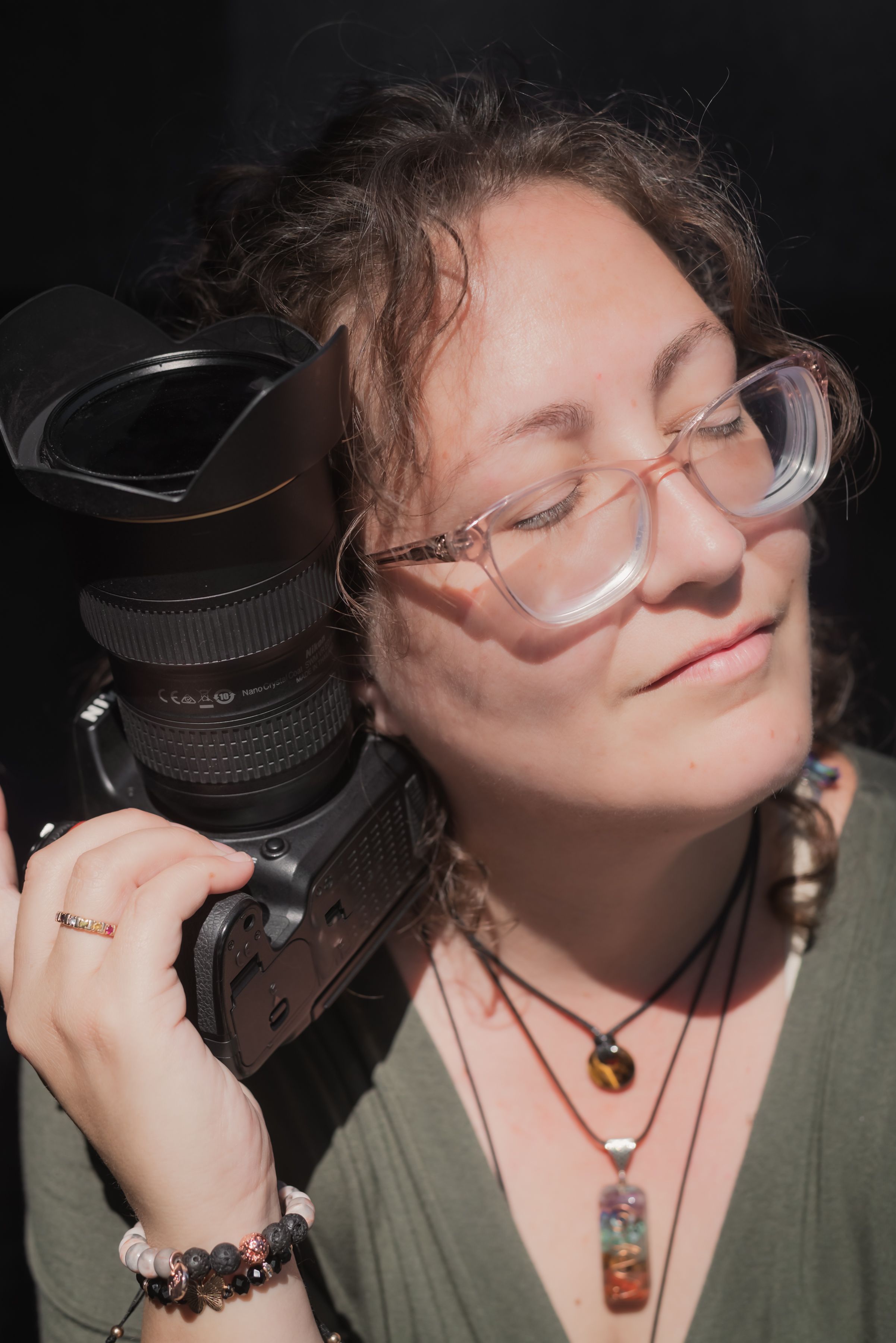 Photographer with glasses smiles while holding camera in natural lighting.