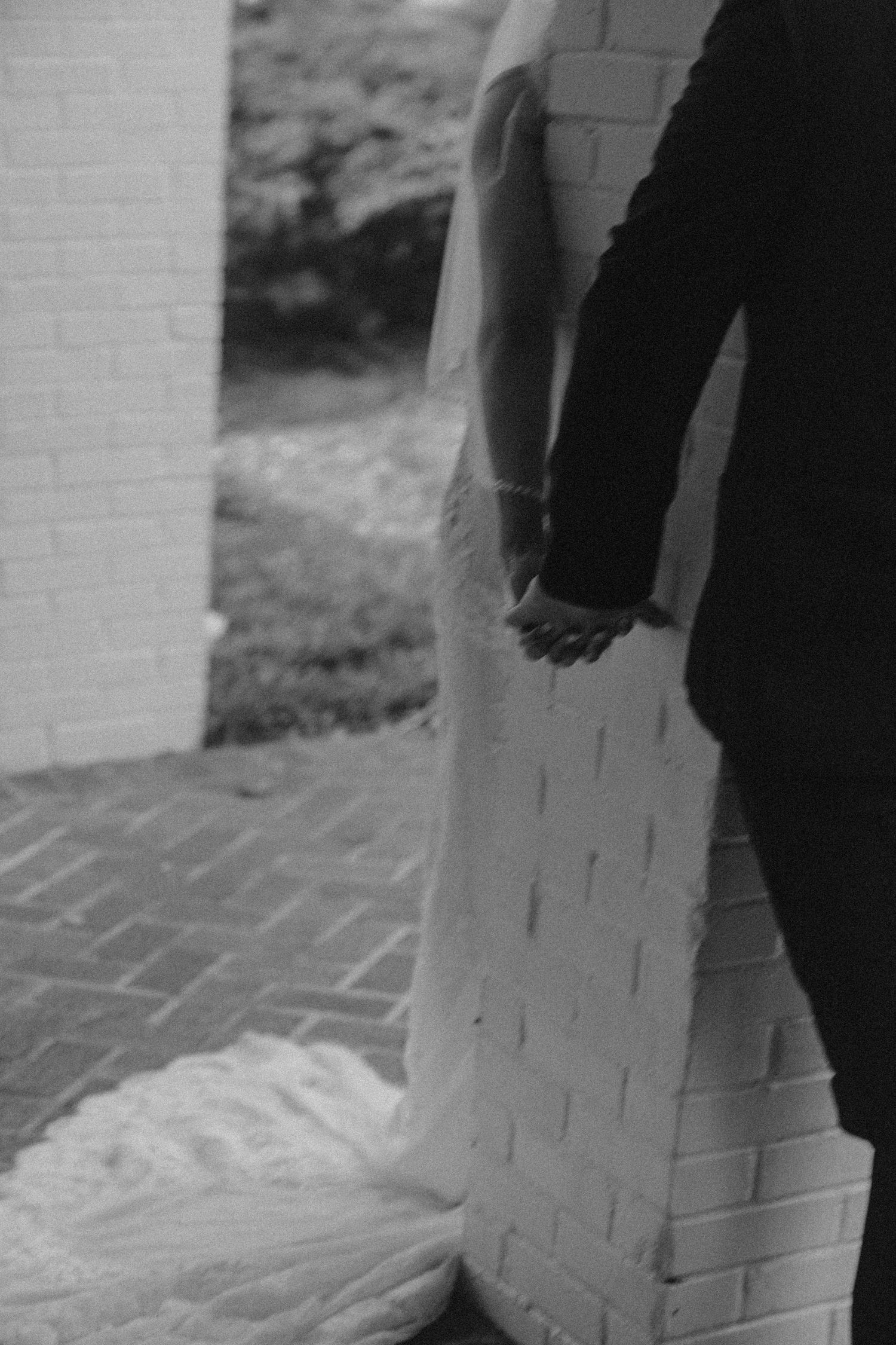 Black and white photo of dress fabric trailing against brick wall.
