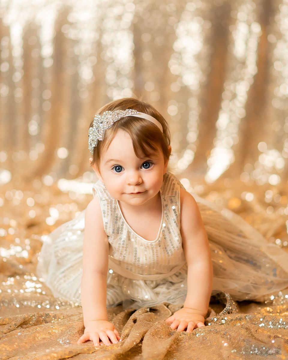 studio portrait of a little girl in a sparkly gold dress on a gold glitter background