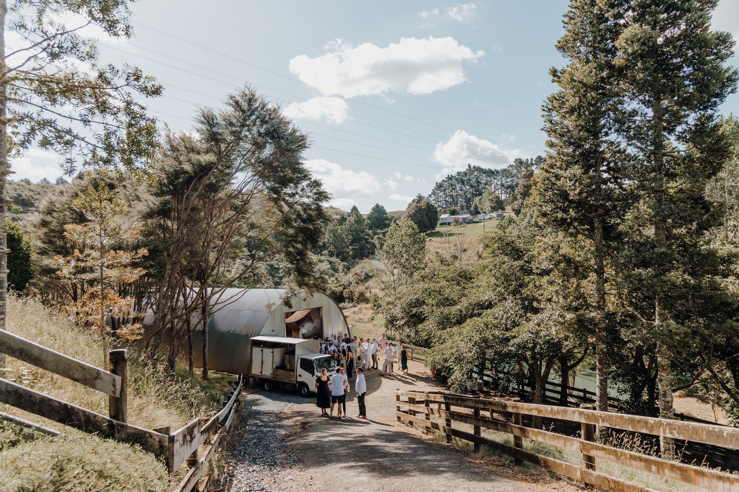 A scenic mountain path leads to a small building surrounded by pine trees on a sunny day.