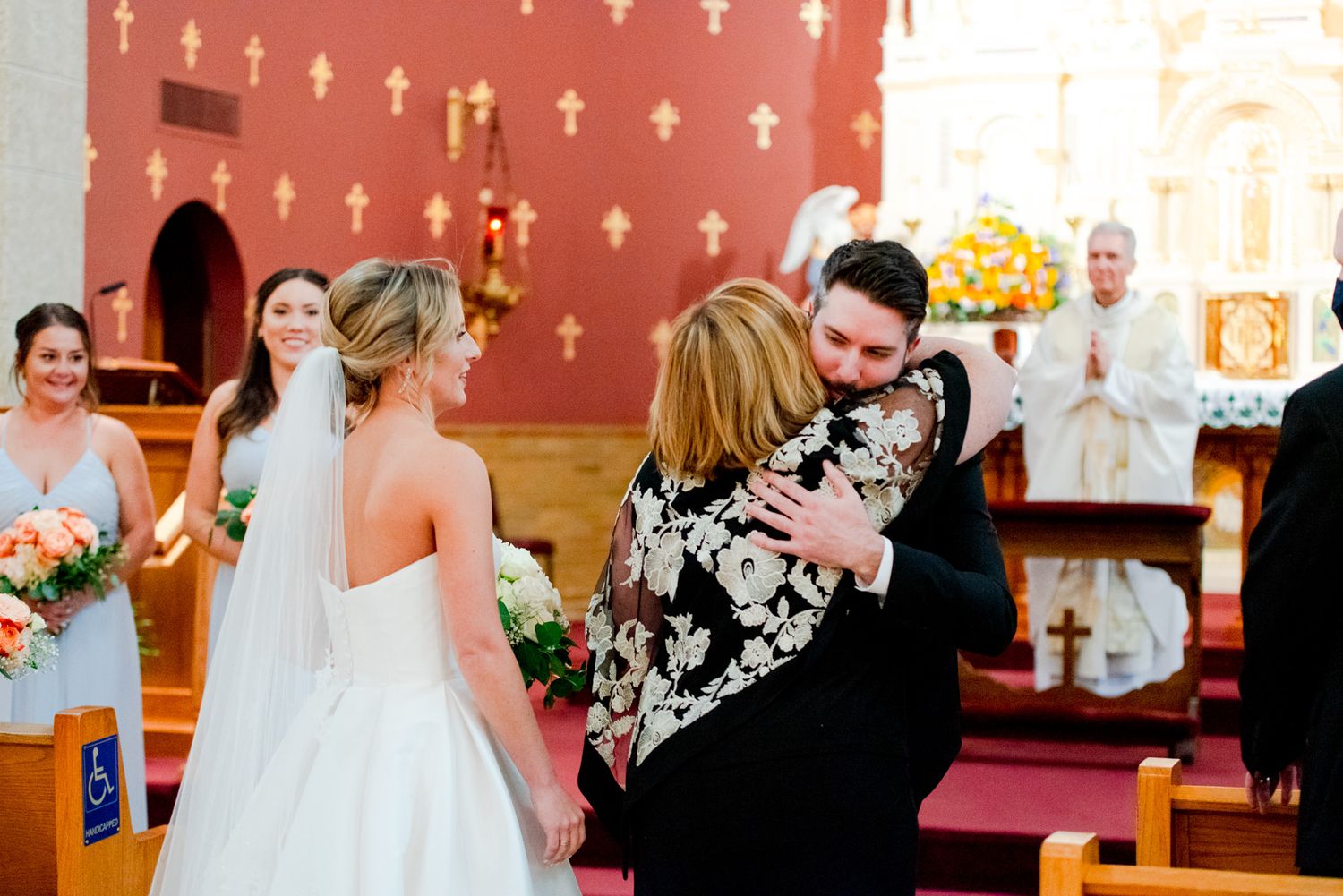 groom and mother of the bride hugging at the church altar before wedding ceremony