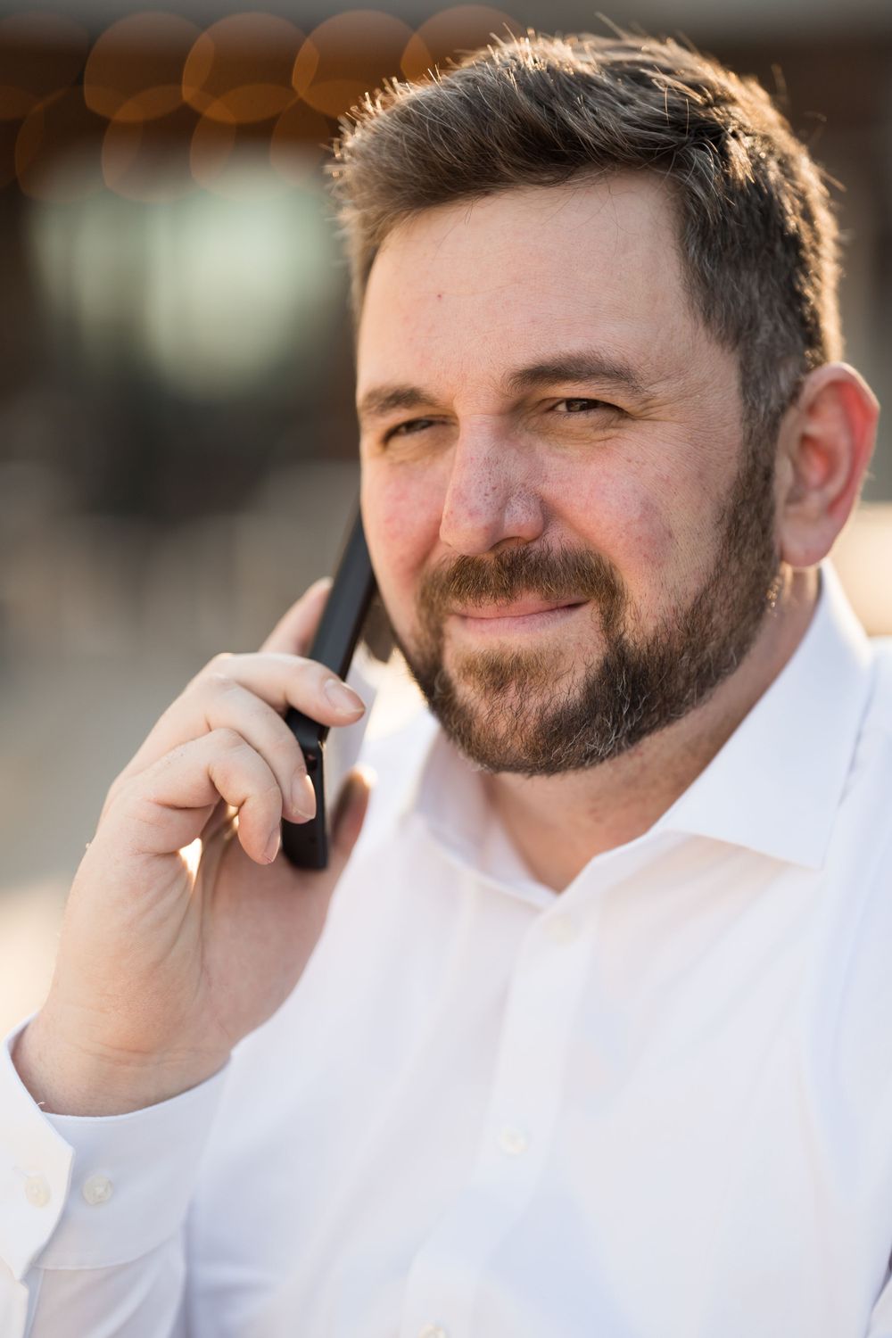 Business casual portrait of person in white shirt talking on phone during golden hour.
