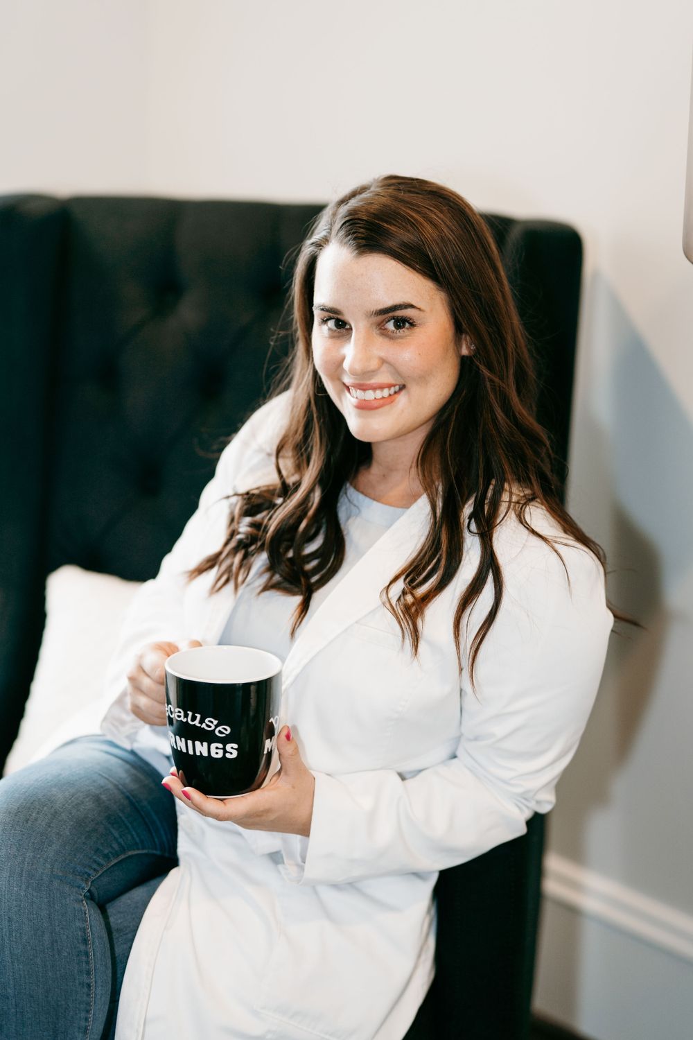 Casual portrait of someone holding coffee mug while sitting in navy armchair.