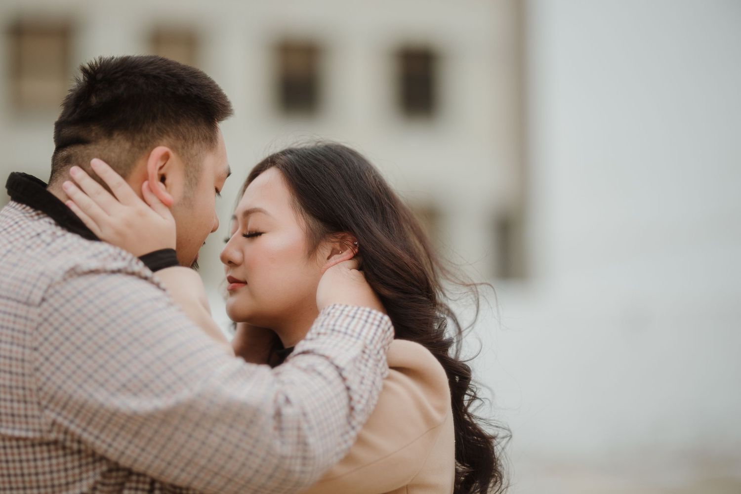 A couple shares a tender romantic moment in front of a building.