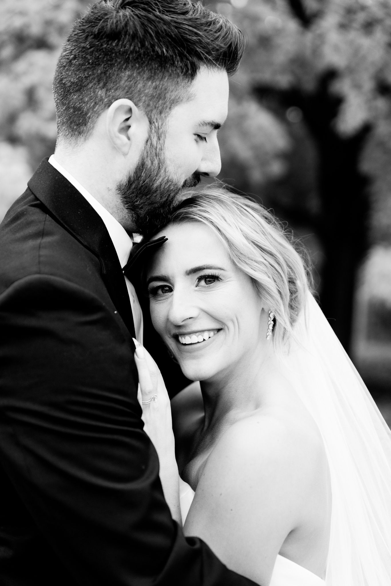 bride lays on grooms chest and smiles at camera while he hugs her