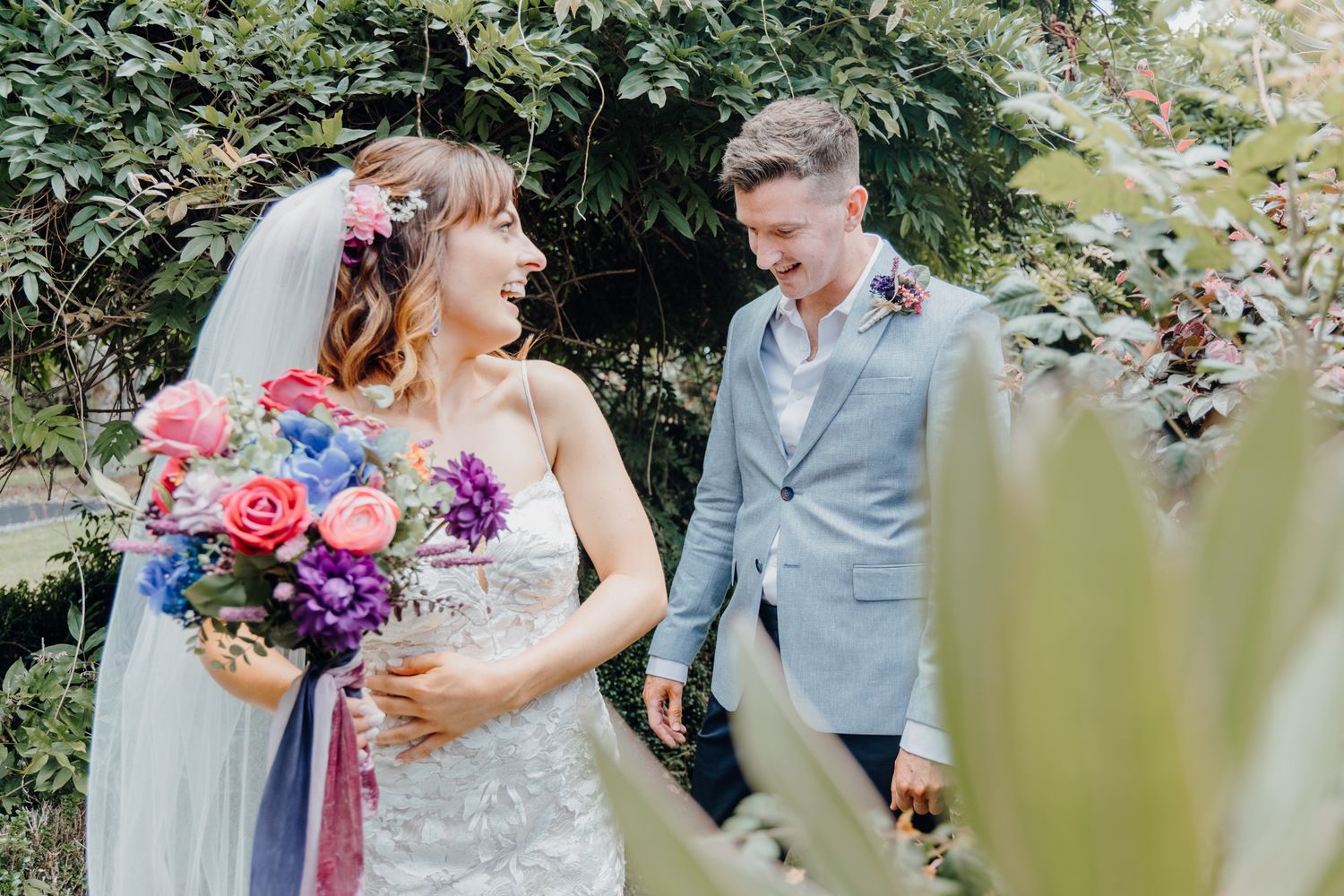 A romantic outdoor wedding moment featuring a vibrant pink and purple bouquet against a lush garden backdrop.