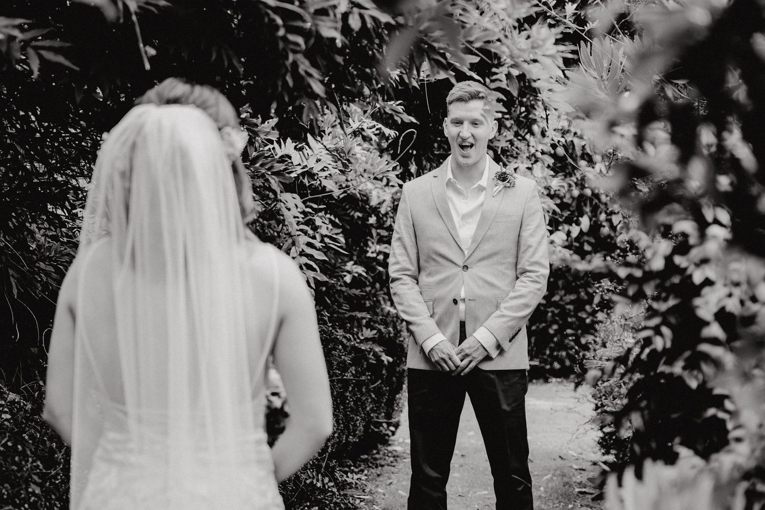 Black and white photo capturing a first look moment between newlyweds on a garden path.