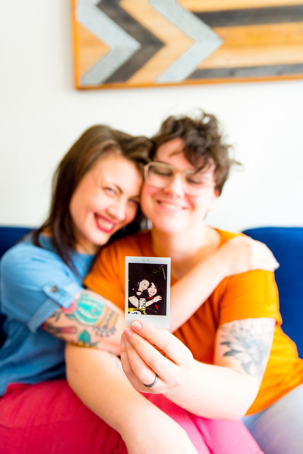 couple holding polaroid of them, in the same pose on their blue couch
