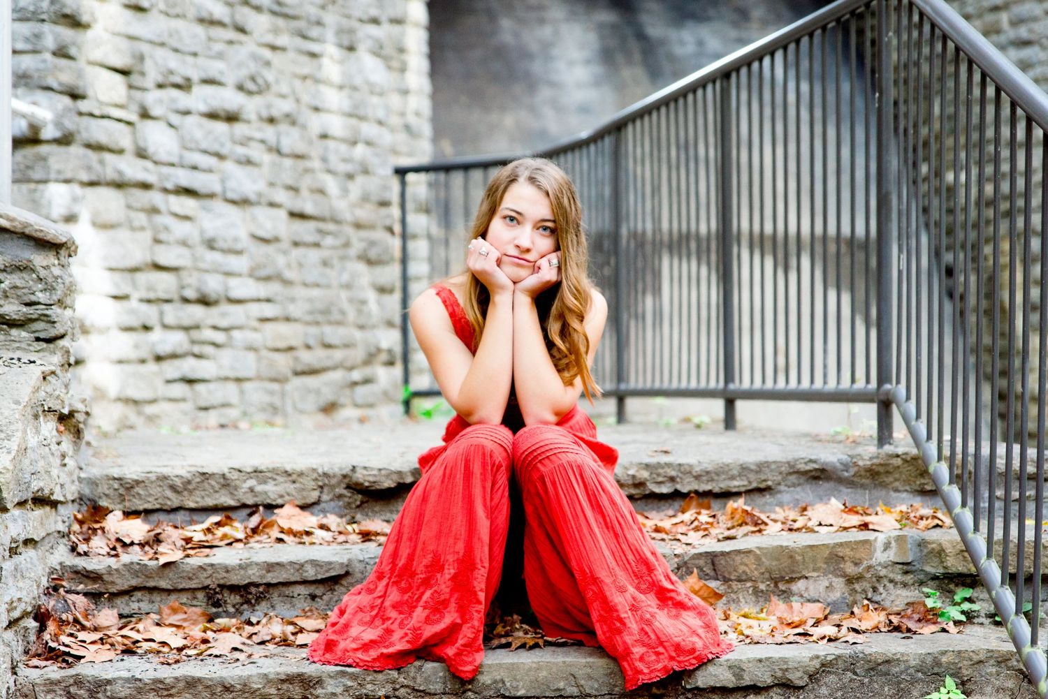young woman in orange jumpsuit sits on stone stairs with leaves on them in the fall for Chicago senior pictures
