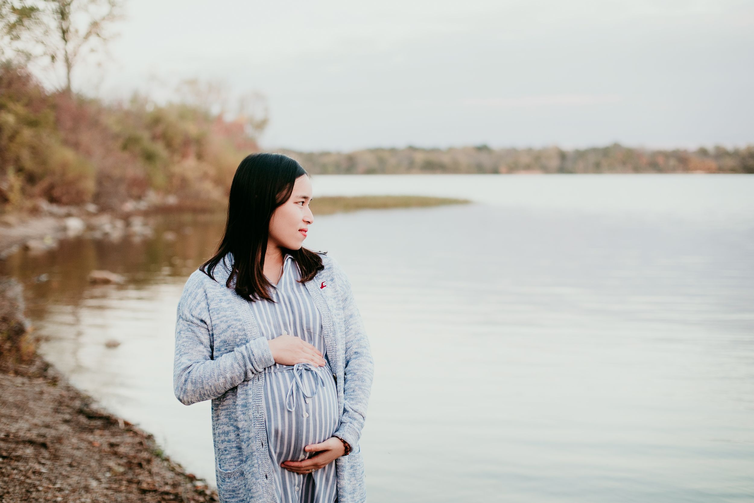 pregnant woman cradling her belly looking out at lake