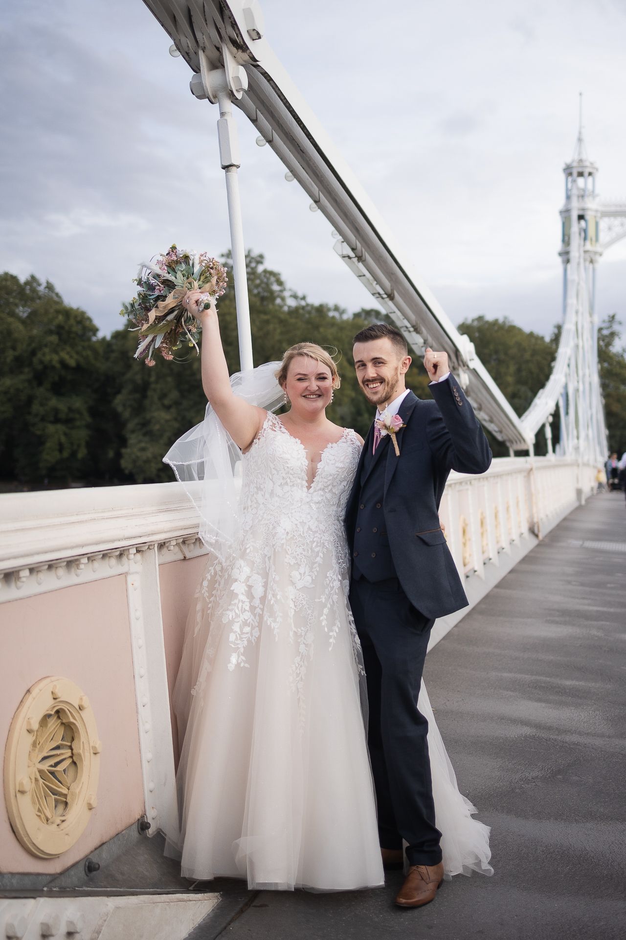 Bride and groom with their hands in the air celebrating their wedding on Albert Bridge, Kensington, London.