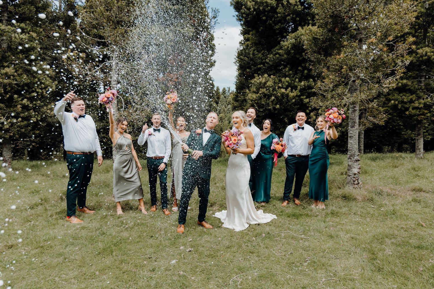 Wedding party celebrates with confetti shower in an outdoor garden setting.