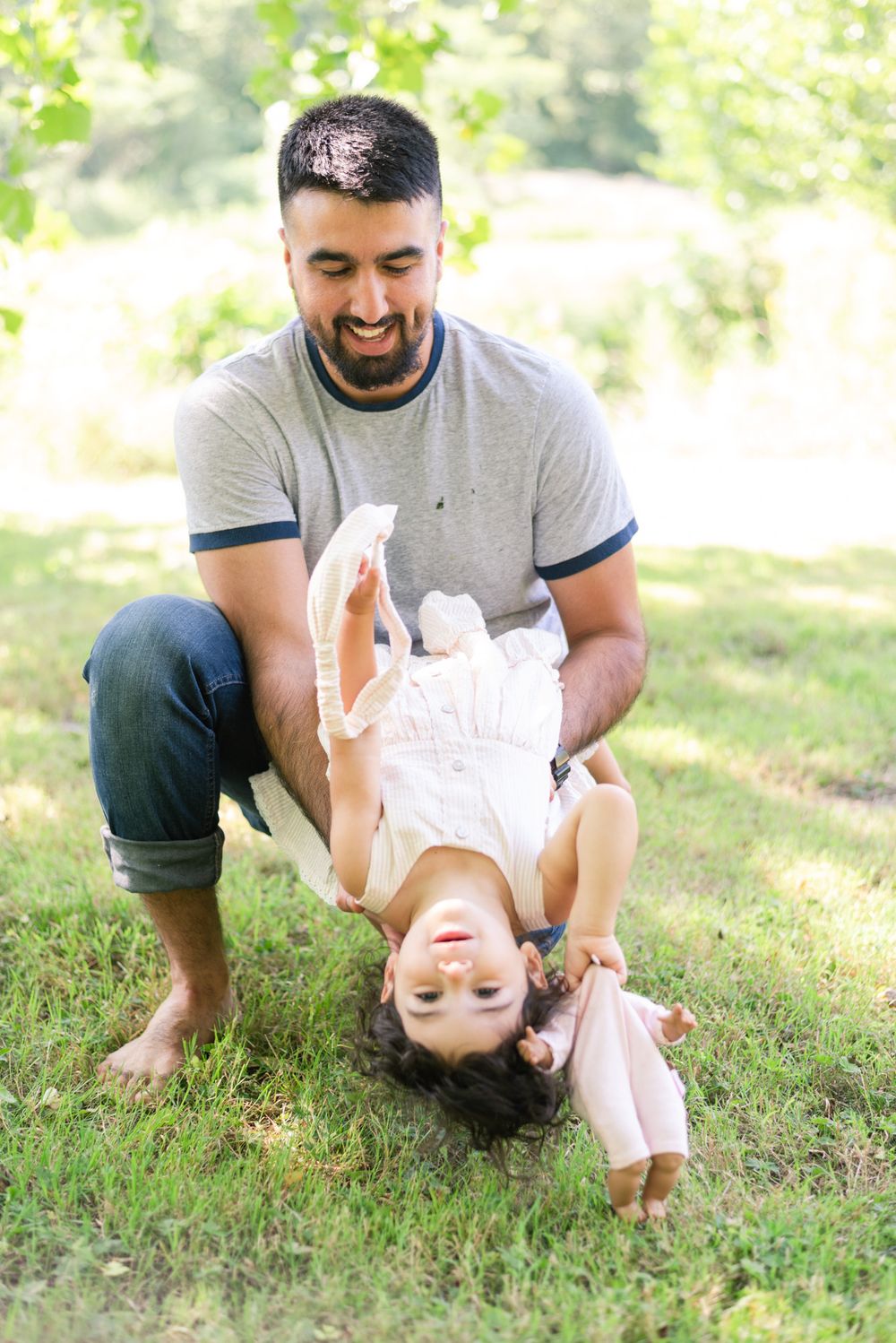 Dad holding daughter upside down in grass in Pittsburgh, Pennsylvania