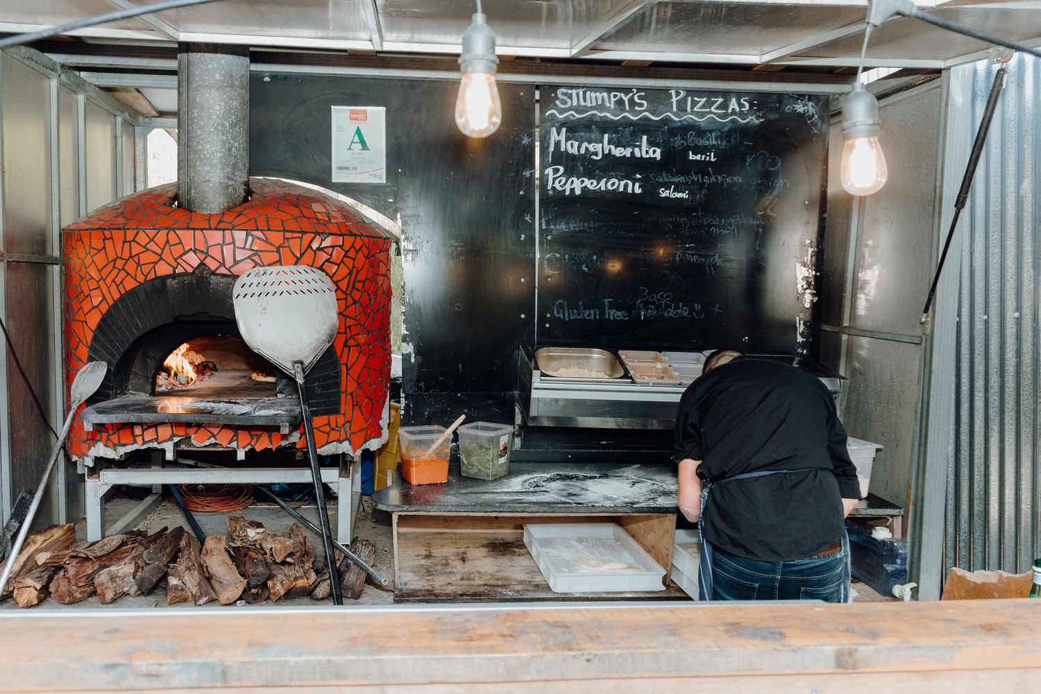 Wood-fired pizza oven with red brick exterior in a rustic kitchen setting.